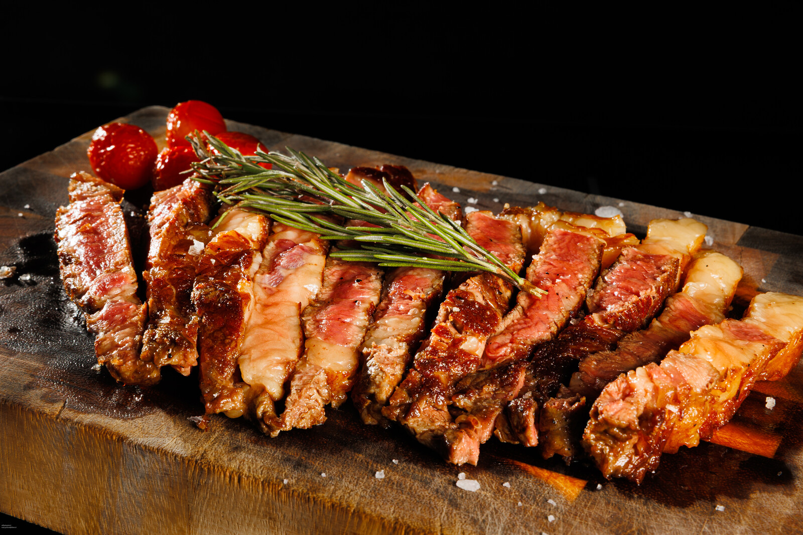 Fette di carne alla brace allineate sul tagliere con rosmarino