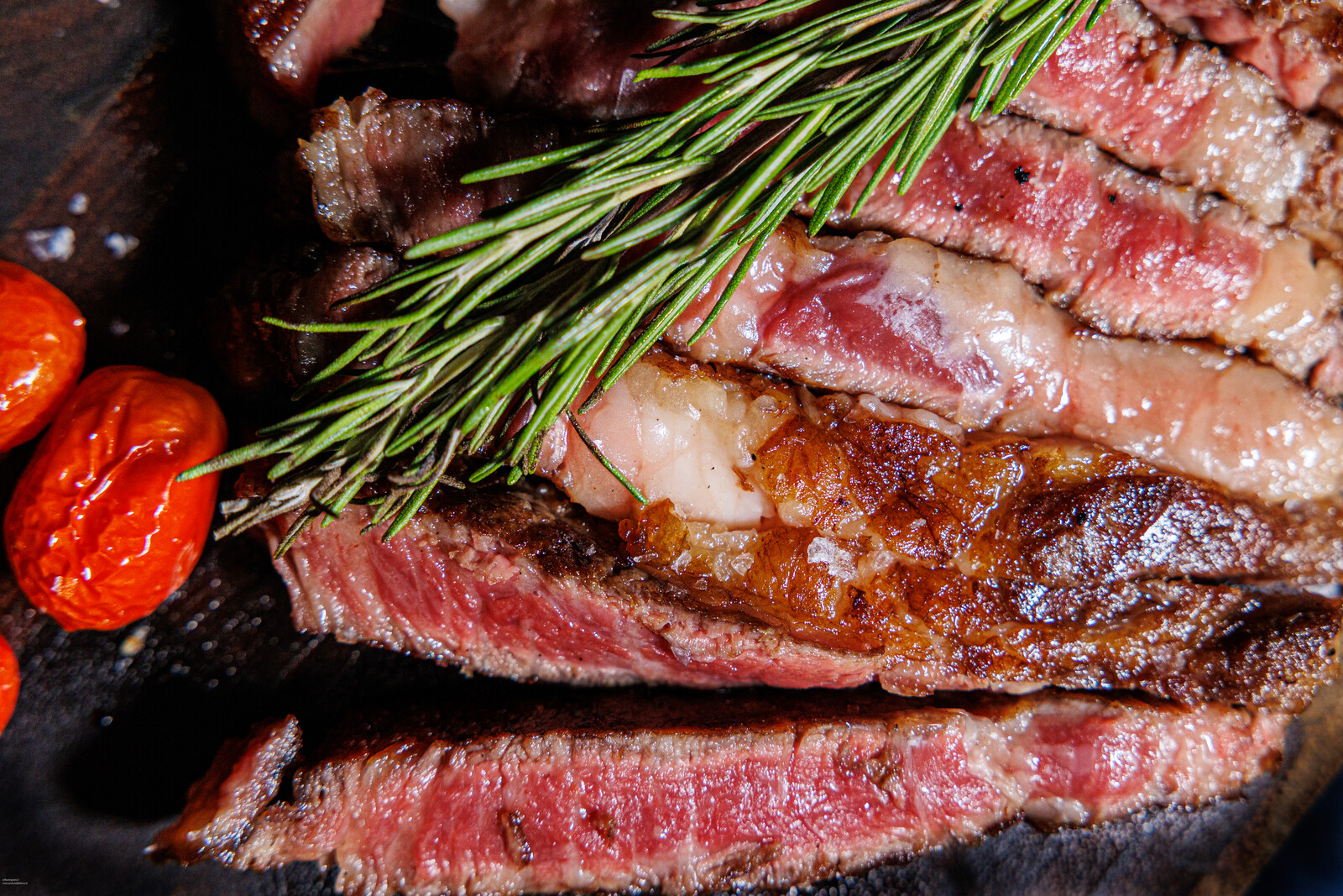Fette di carne alla brace viste da vicino, con erbe e pomodorini
