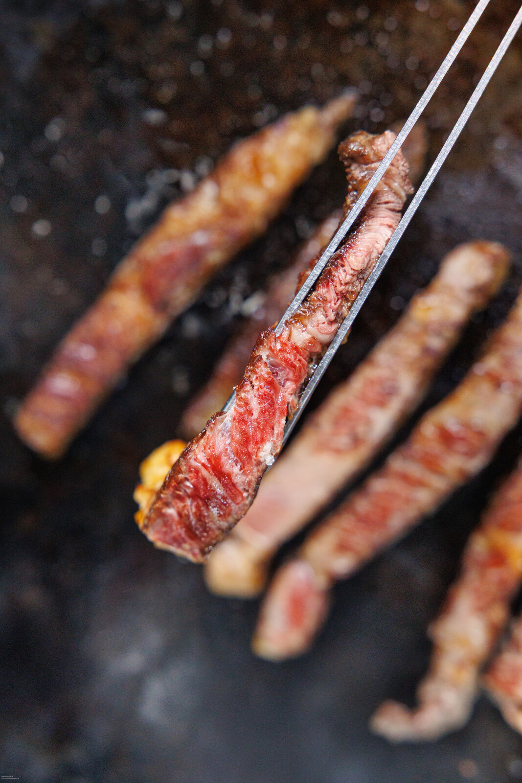 Fettine di carne scottata prese con la pinza su una piastra scura