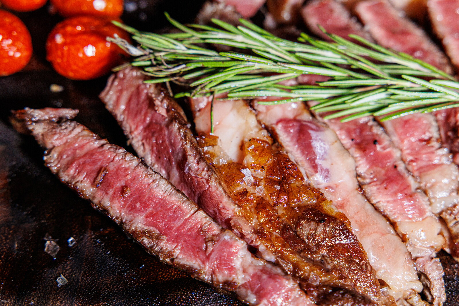 Primo piano di fette di carne al sangue con pomodorini e rosmarino