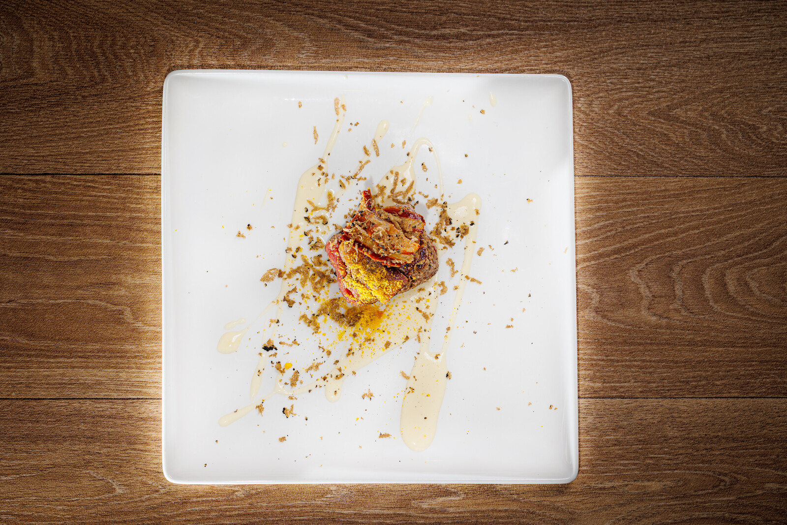Piatto quadrato bianco con un bocconcino di carne e briciole croccanti