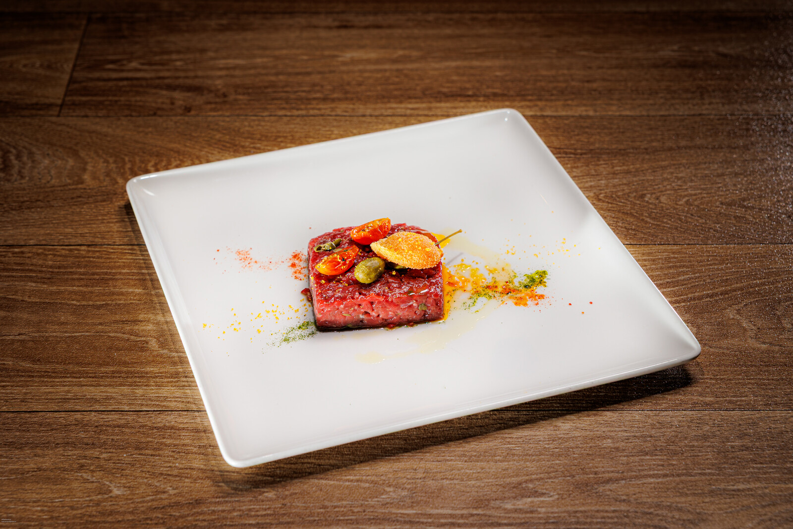 Piatto rettangolare bianco con un bocconcino di carne e salse