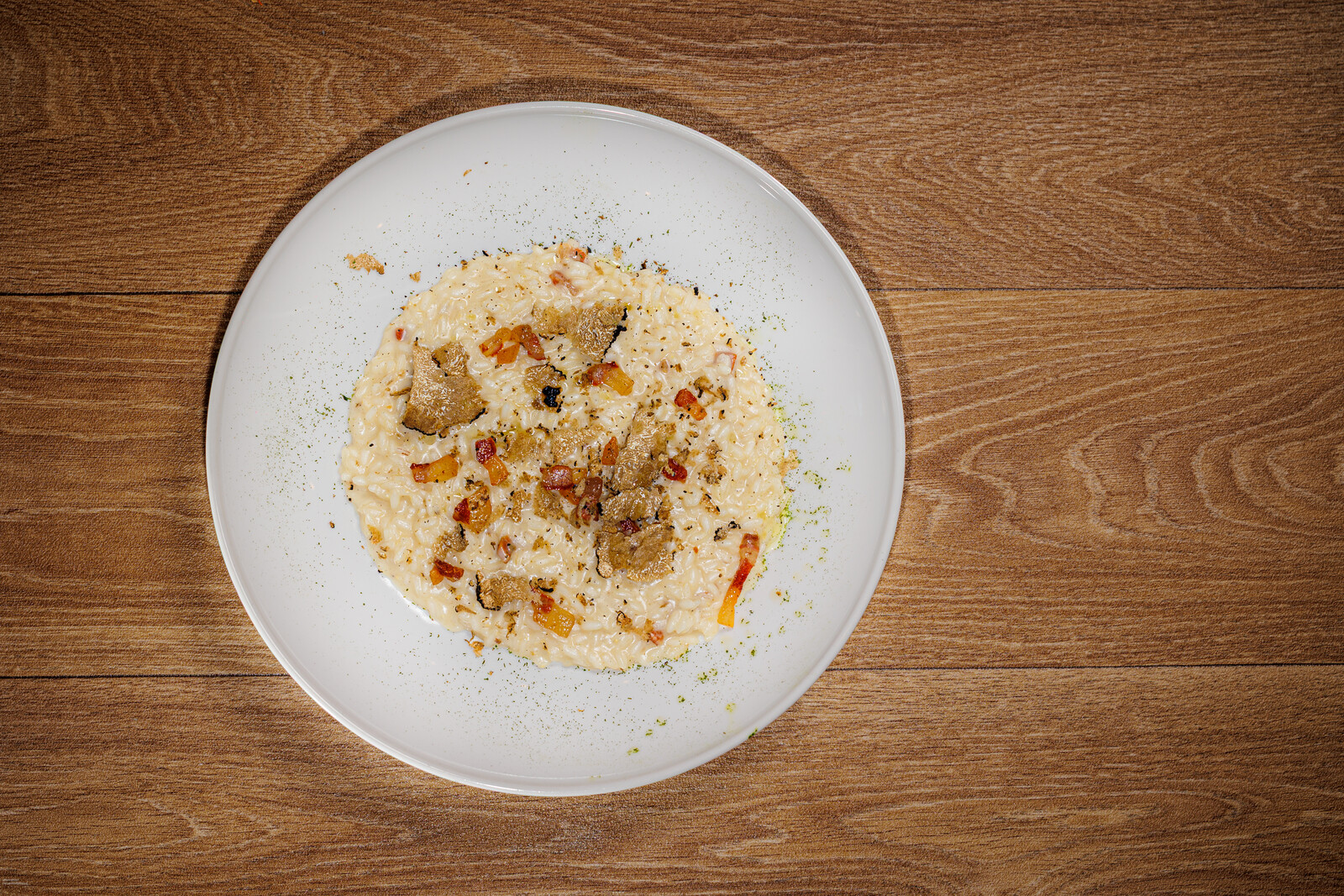 Risotto con tartufo nero e dadini di speck su piatto bianco